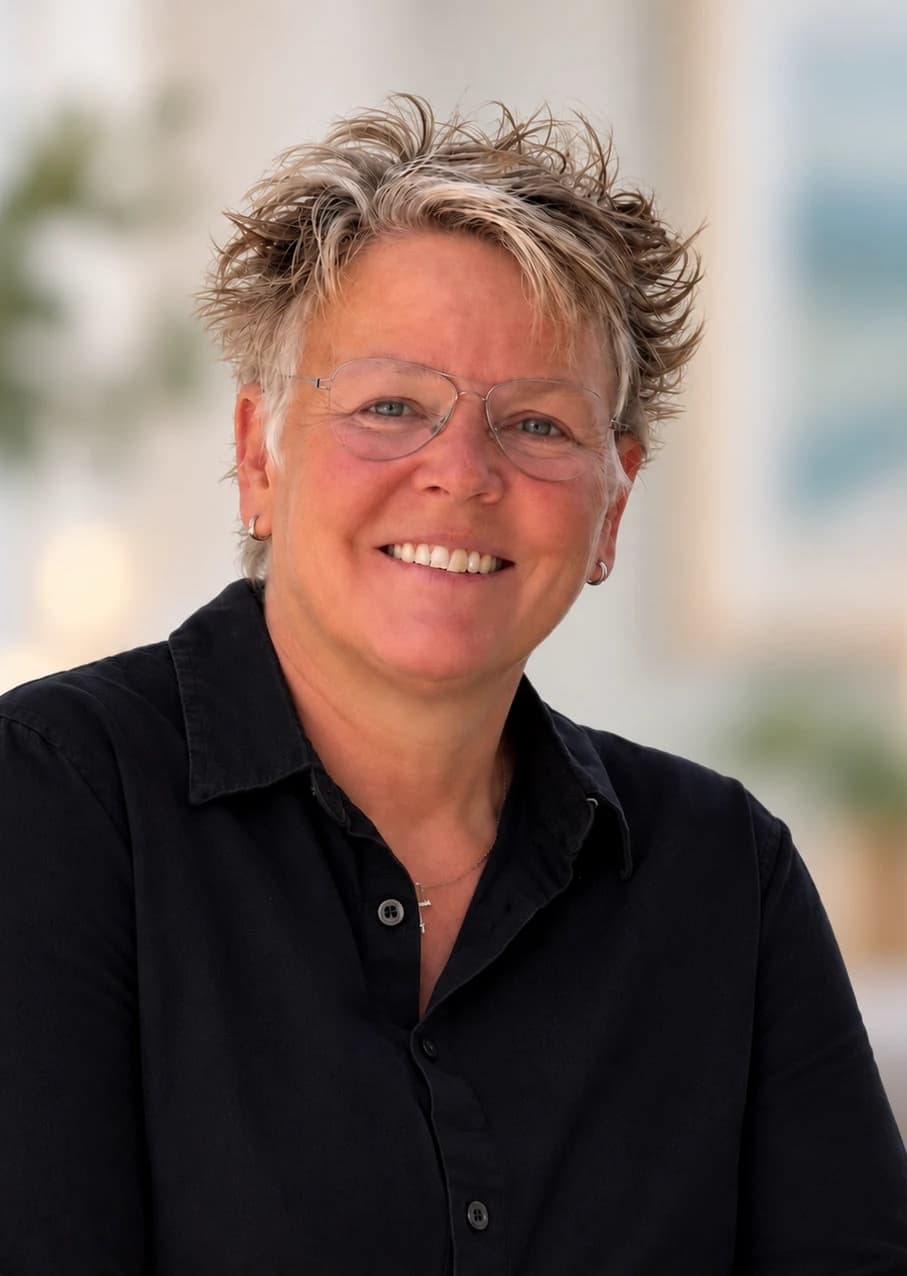 Caroline, lachend, met een bril en een donker overhemd.